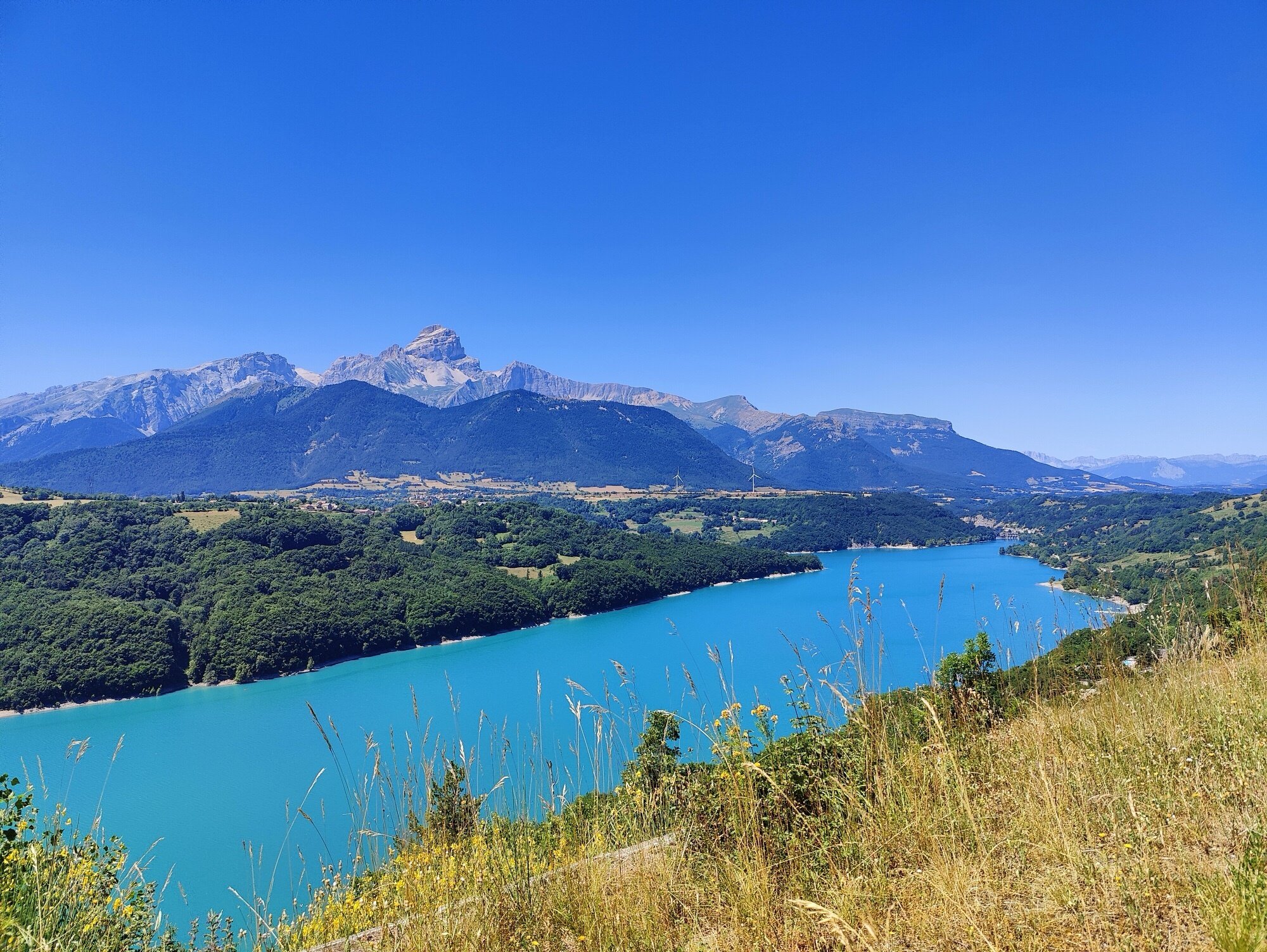 Vue plongeante sur le Lac du Sautet depuis la route, les contreforts des Écrins à l'horizon