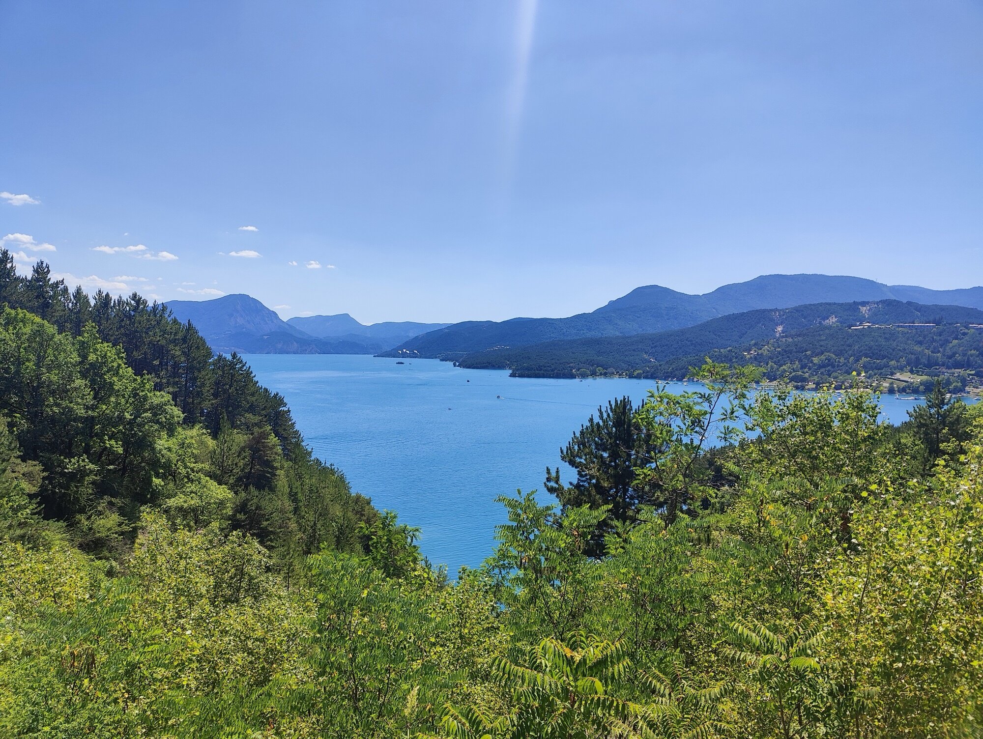Premier éclat de Serre-Ponçon entre les pins — un bleu méditerranéen impossible à 800 mètres